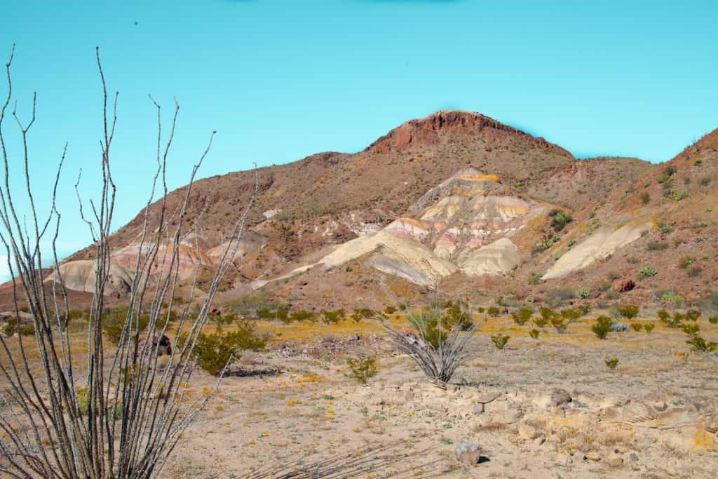 a desert landscape with a mountain and blue sky