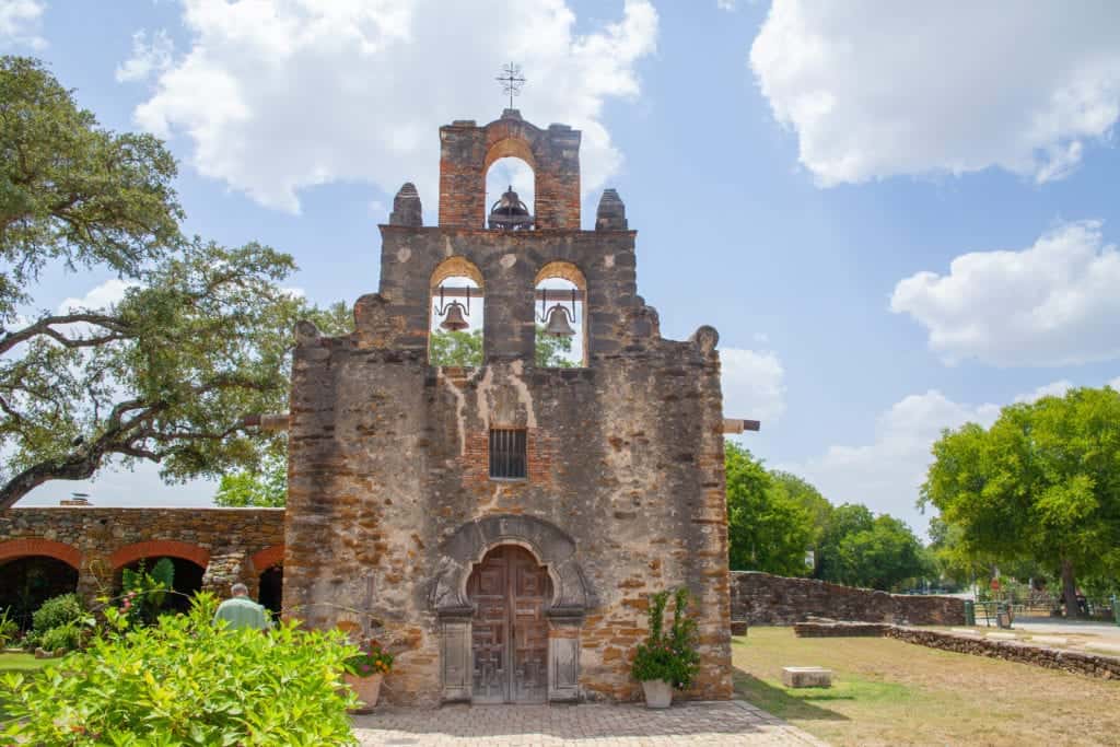 Historic stone mission building with bell towers under blue skies.