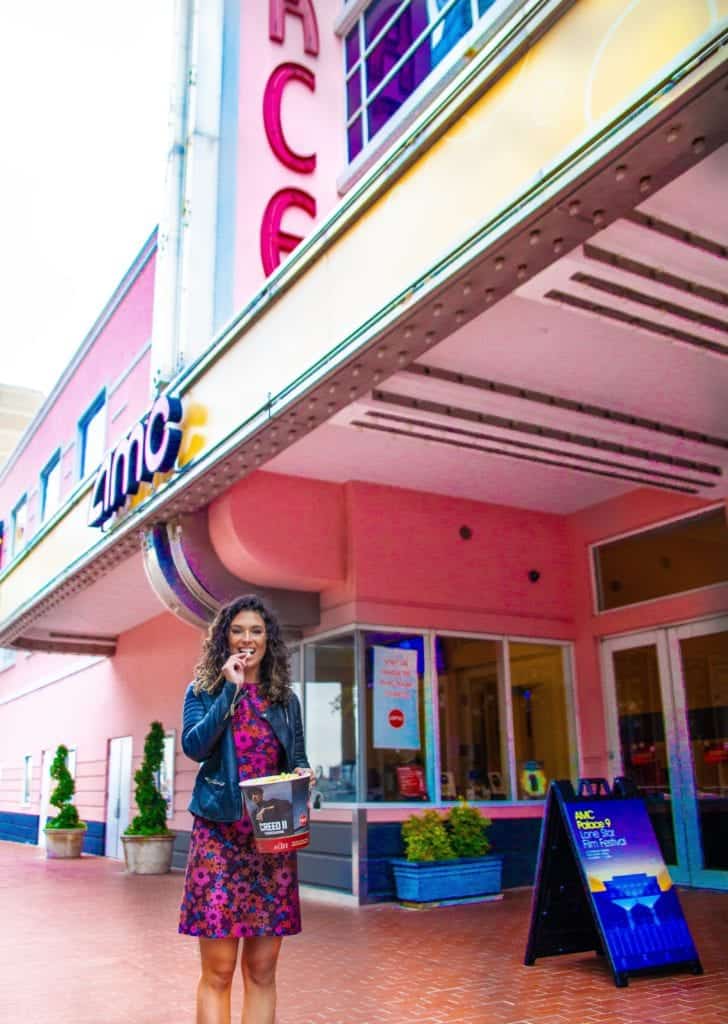 A woman poses in front of a pink building