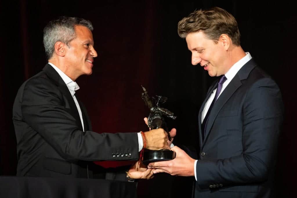 Two men in suits shake hands at an award ceremony