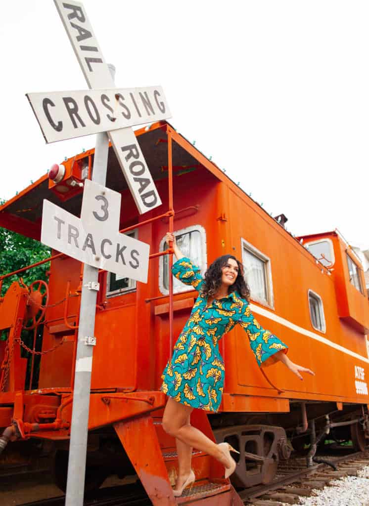 a person posing in front of a railroad crossing sign