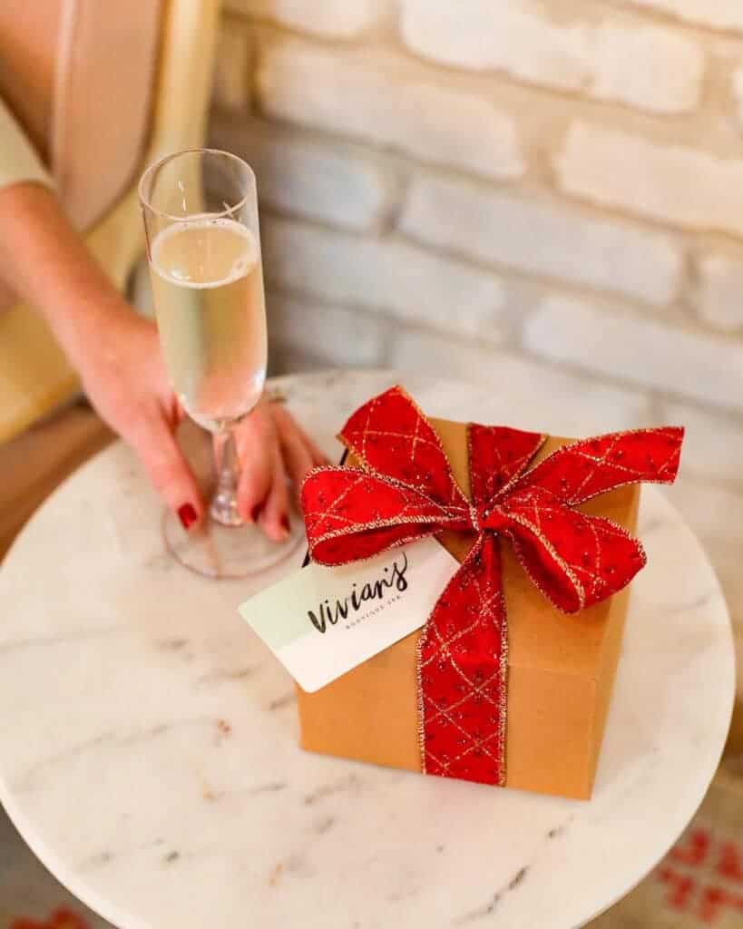 a hand holding a glass of champagne next to a gift box