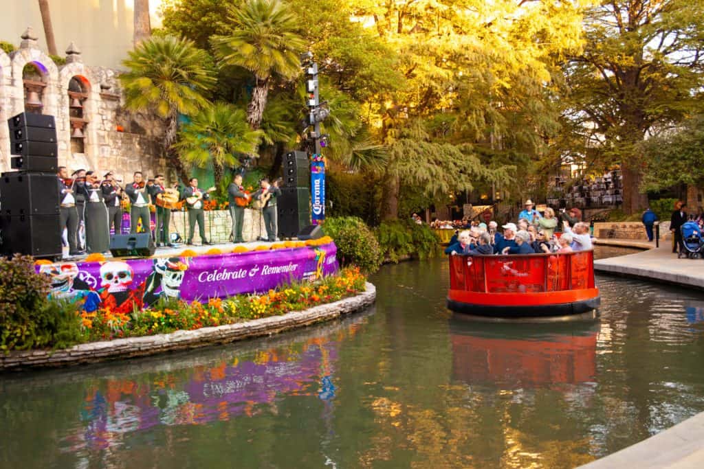 a group of people on a boat with San Antonio River Walk in the background