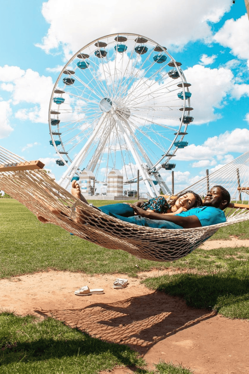 A couple enjoying a relaxing moment in a hammock with a giant ferris wheel on the background