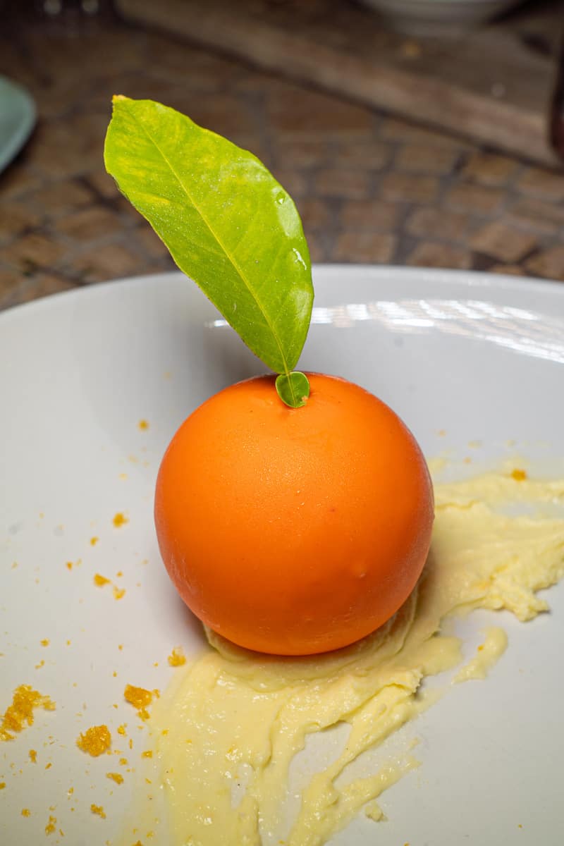 A dessert that looks like an orange with a leaf coming out of the top on a white plate