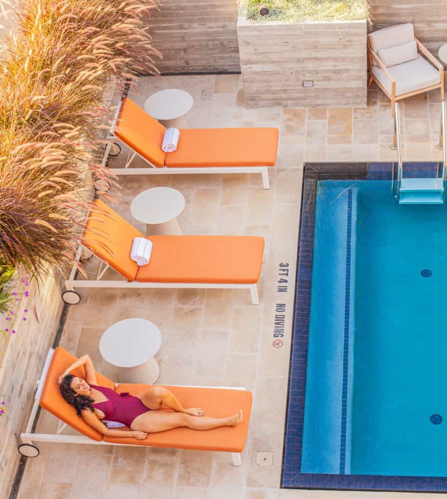 A woman relaxes in a purple swimsuit on a lounge chair by a swimming pool at Canopy Hotel