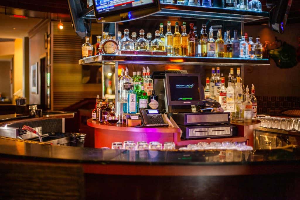 A bar featuring a television screen and a variety of alcohol bottle