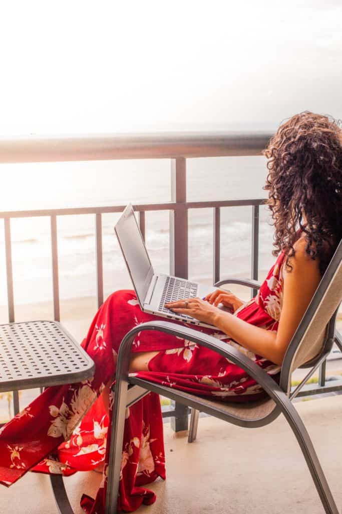 Jessica in a red dress sits on a chair, working on a laptop.