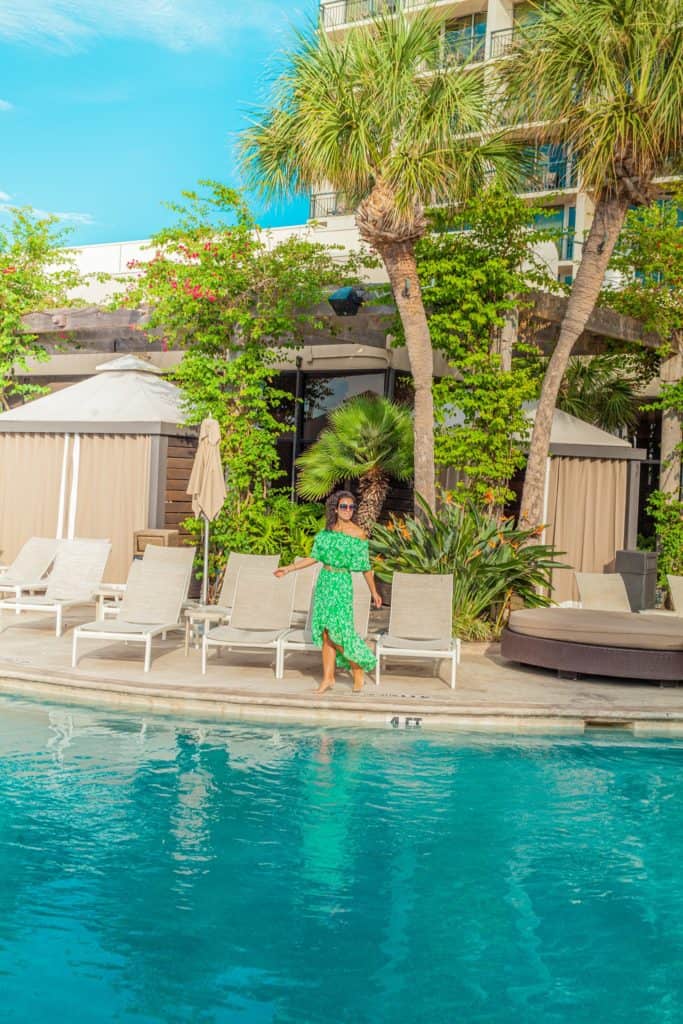 Jessica in a green dress stands by the pool at a resort
