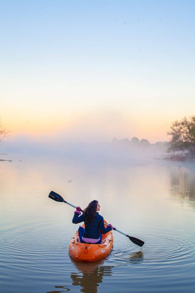 A woman paddles a kayak on a calm lake