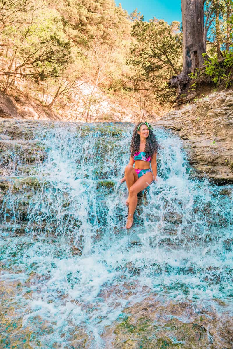 A woman in a bikini enjoying the refreshing waterfall, surrounded by lush greenery and a serene atmosphere.