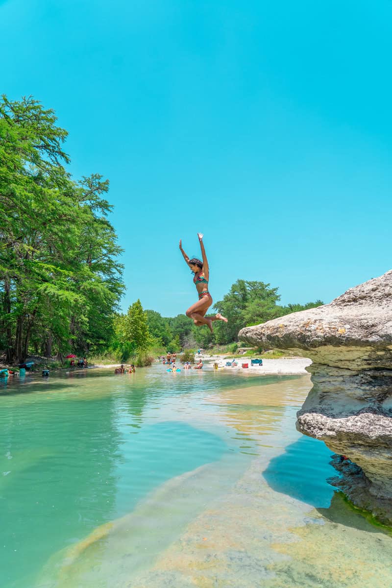 A woman joyfully diving into a serene lake, surrounded by nature's beauty.