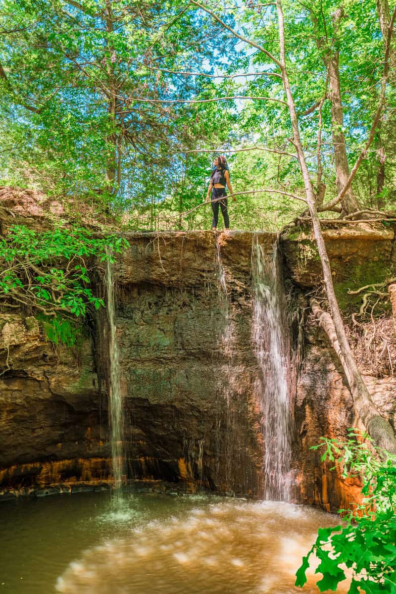 A woman enjoying the view of a waterfall while standing on a rock.