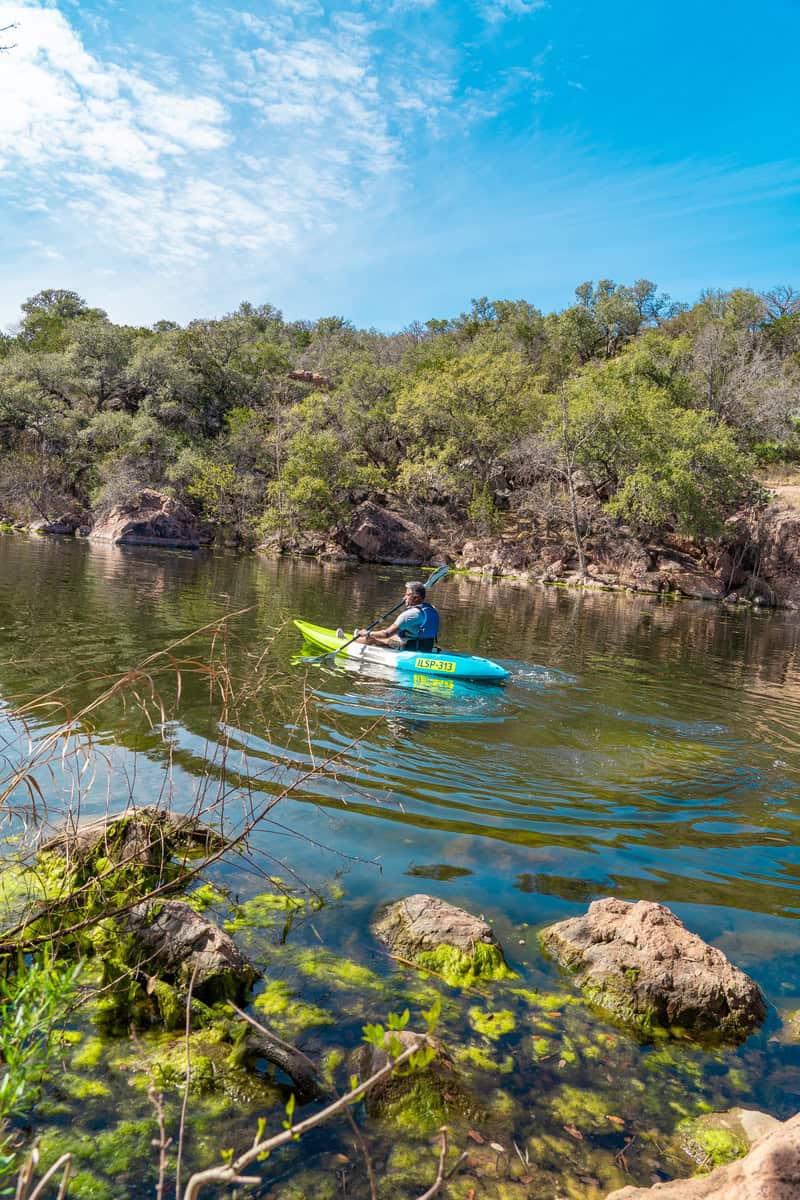 A man paddling a kayak on serene water.