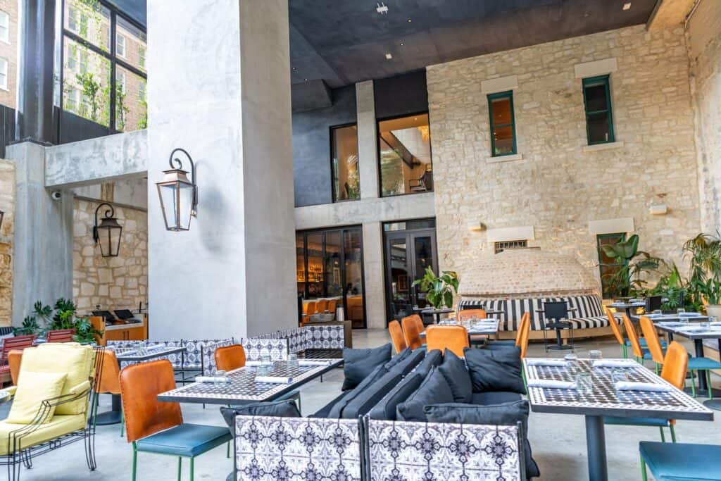 Modern restaurant interior featuring stone walls, vibrant patterned seating, and lush greenery at the Canopy by Hilton