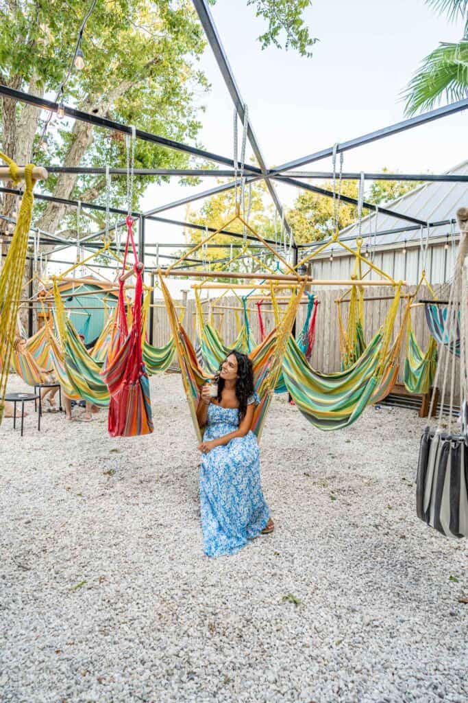 A woman in a blue floral dress sits among colorful hammocks