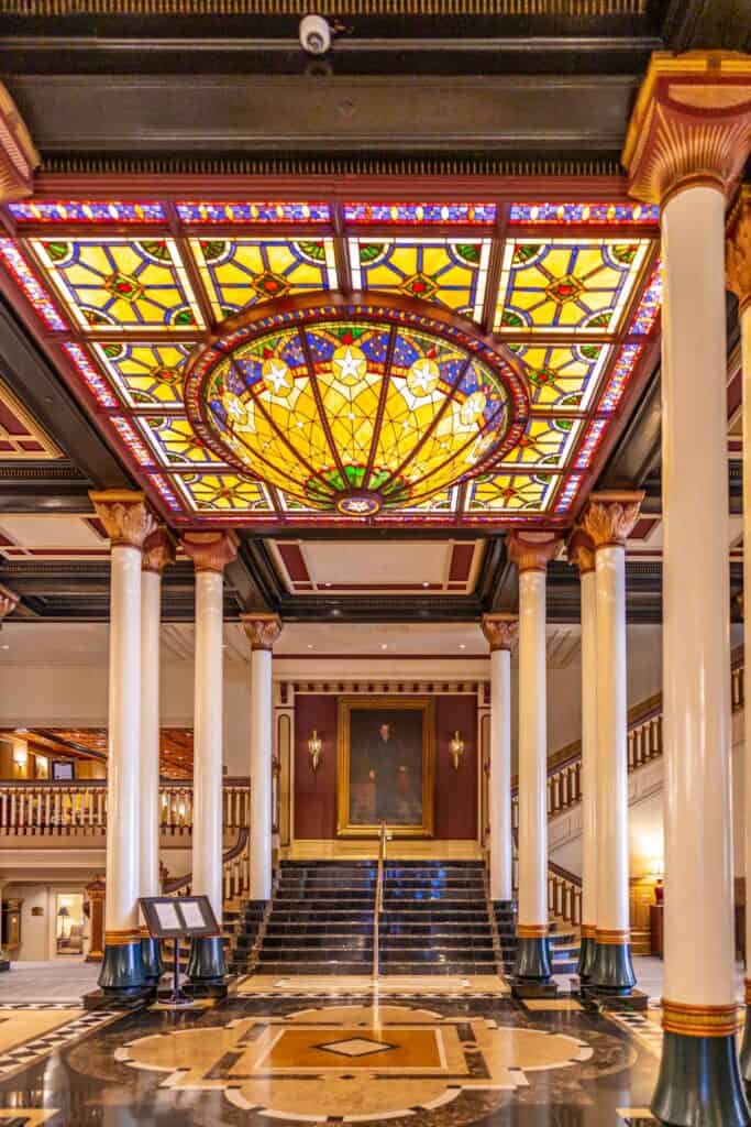 Grand lobby with ornate stained glass ceiling, marble floors, and columns