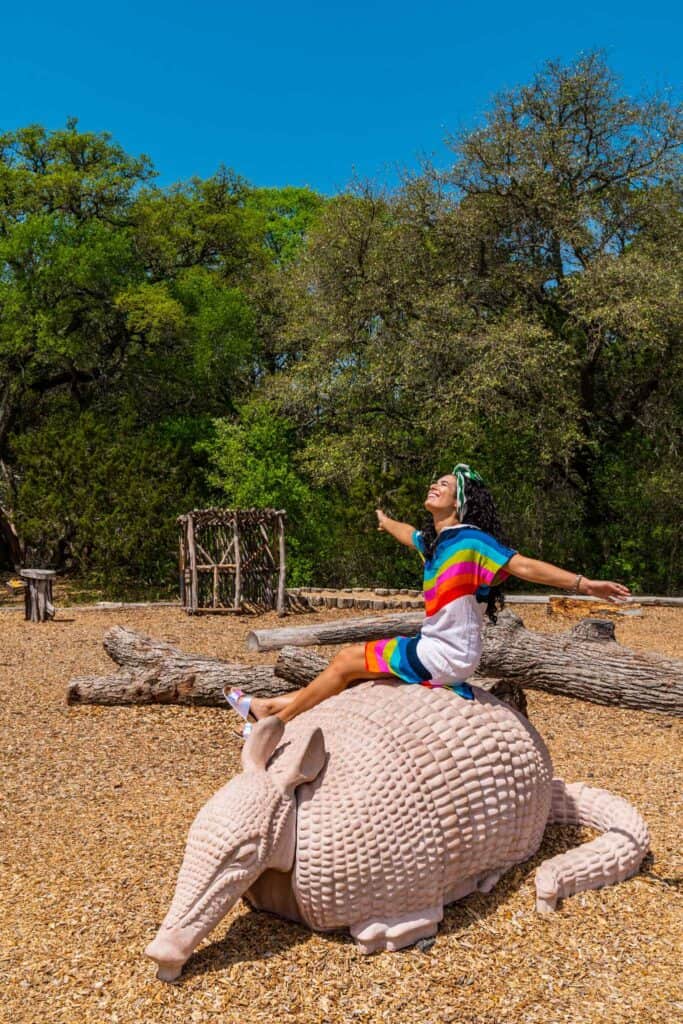 Jessica sitting on an armadillo statue on the playground at Mother Neff State Park in Belton Things to do