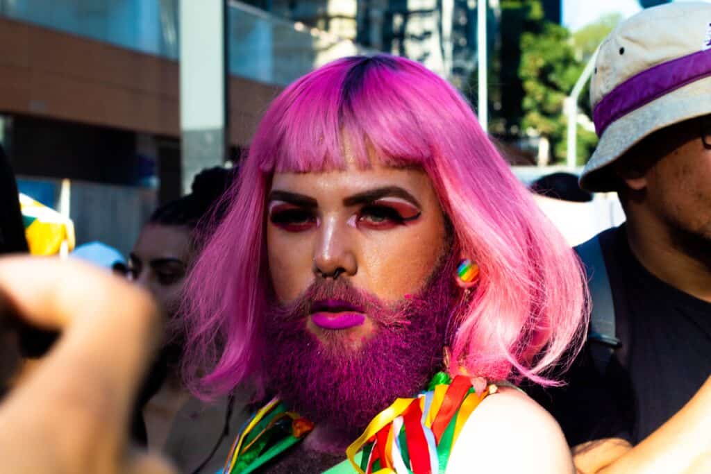 An individual with pink hair, a pink beard, and striking eye make-up