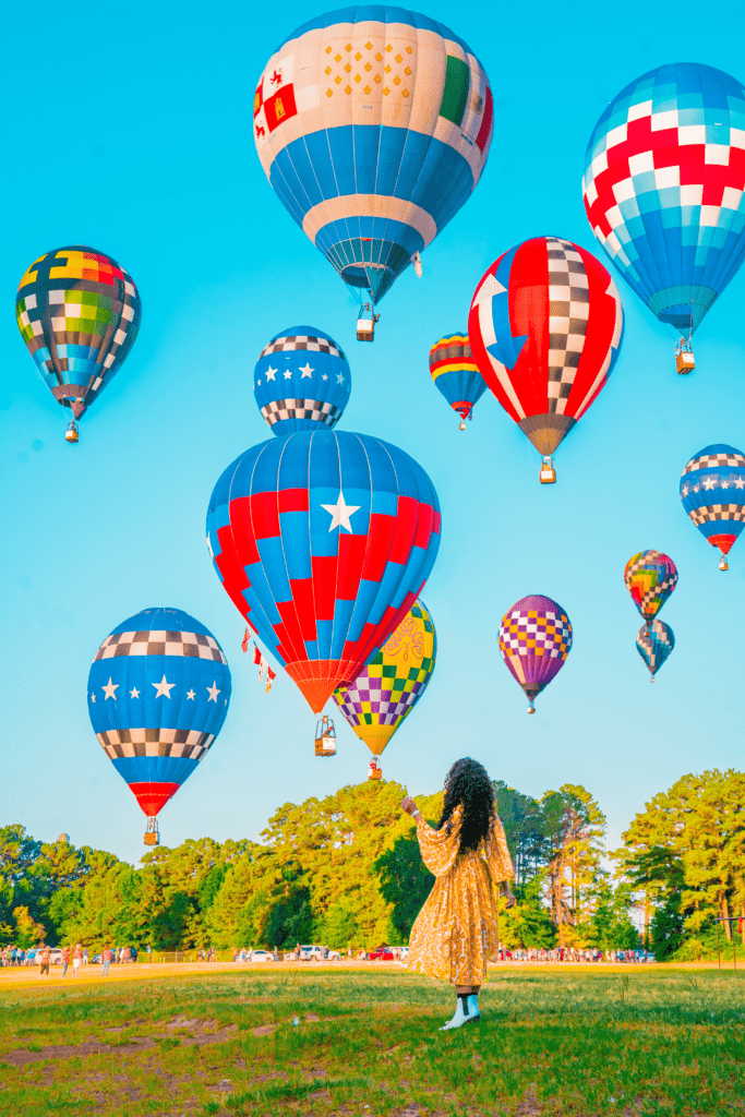 A woman stands in a vibrant field, surrounded by colorful hot air balloons