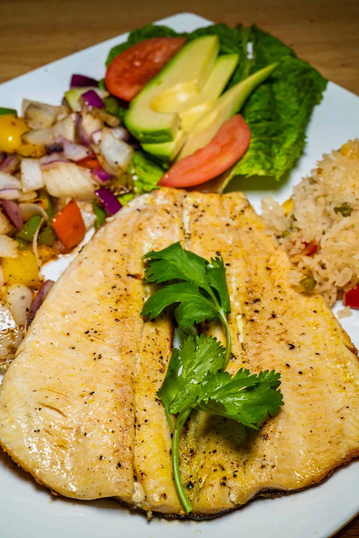 flaky rainbow trout served with sauteed red onions and bell peppers, sliced avocado, and a rice dish with peas and sweet corn