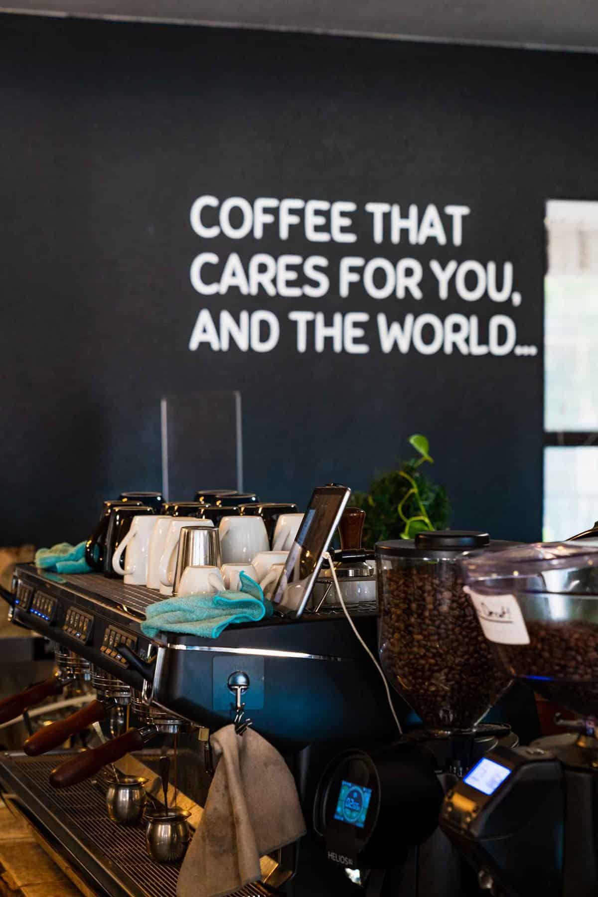 "COFFEE THAT CARES FOR YOU AND THE WORLD" Sign with Coffee Machine on background