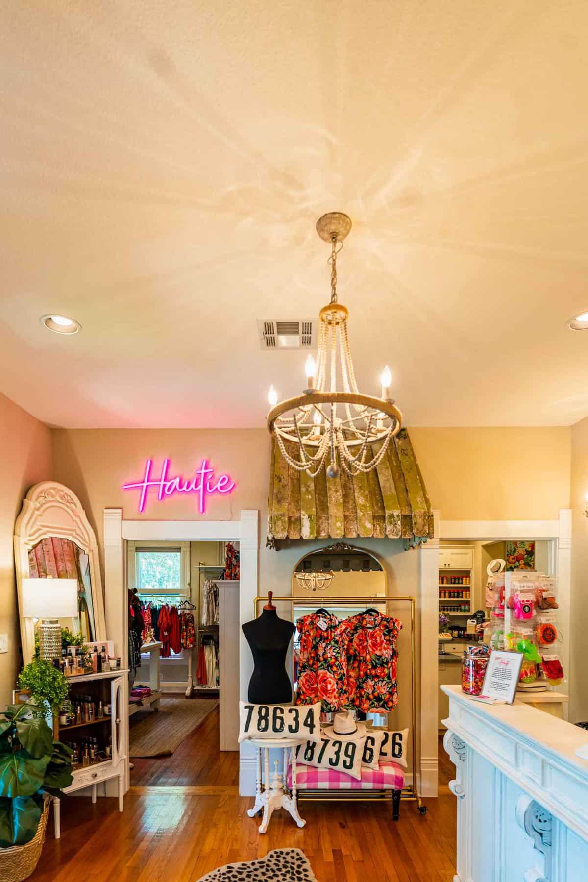 Boutique interior with chandelier, clothes on display and "Hautie" neon sign