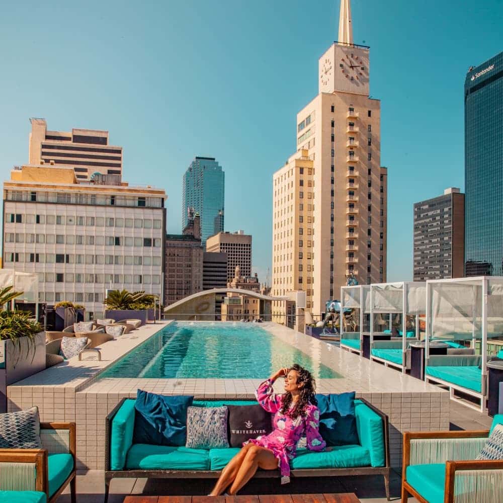 Woman sitting on a rooftop deck with a pool and skyscrapers in the background