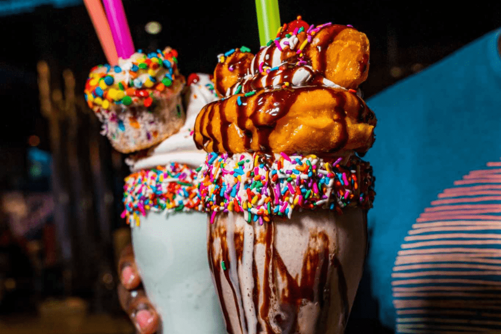 Shake topped with two donuts from and Birthday Cake shake, topped with a whole cupcake and a matching sprinkle-covered rim