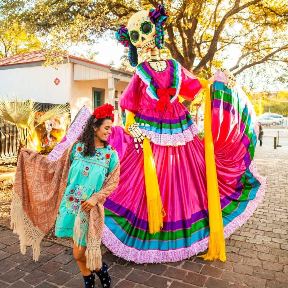 Woman standing next to a tall skeleton dressed in a traditional Mexican dress