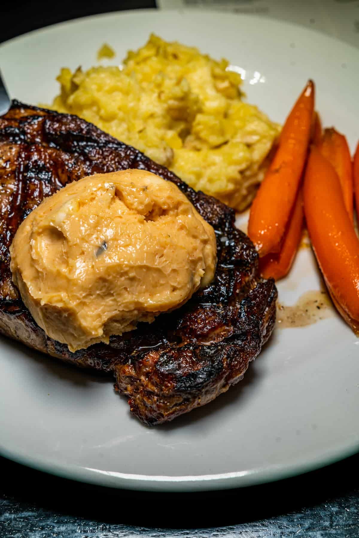 Steak with herb butter, mashed potatoes, and carrots