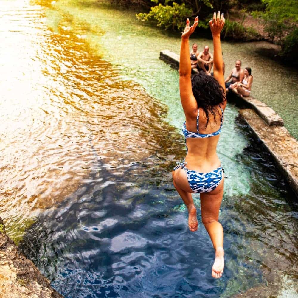 Woman jumping off a rock into swimming hole