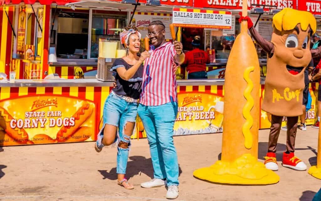 Couple with corn dogs in front of the Fletcher's Corny Dog booth