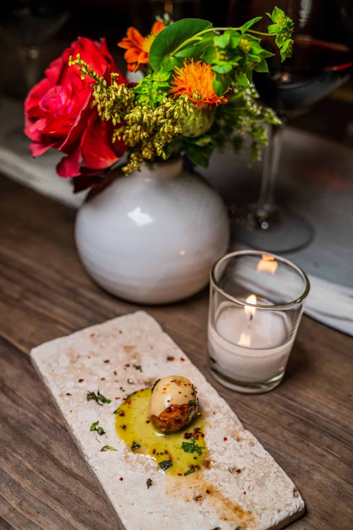 Quail egg on a platter flanked by vase of flowers and a lit candle