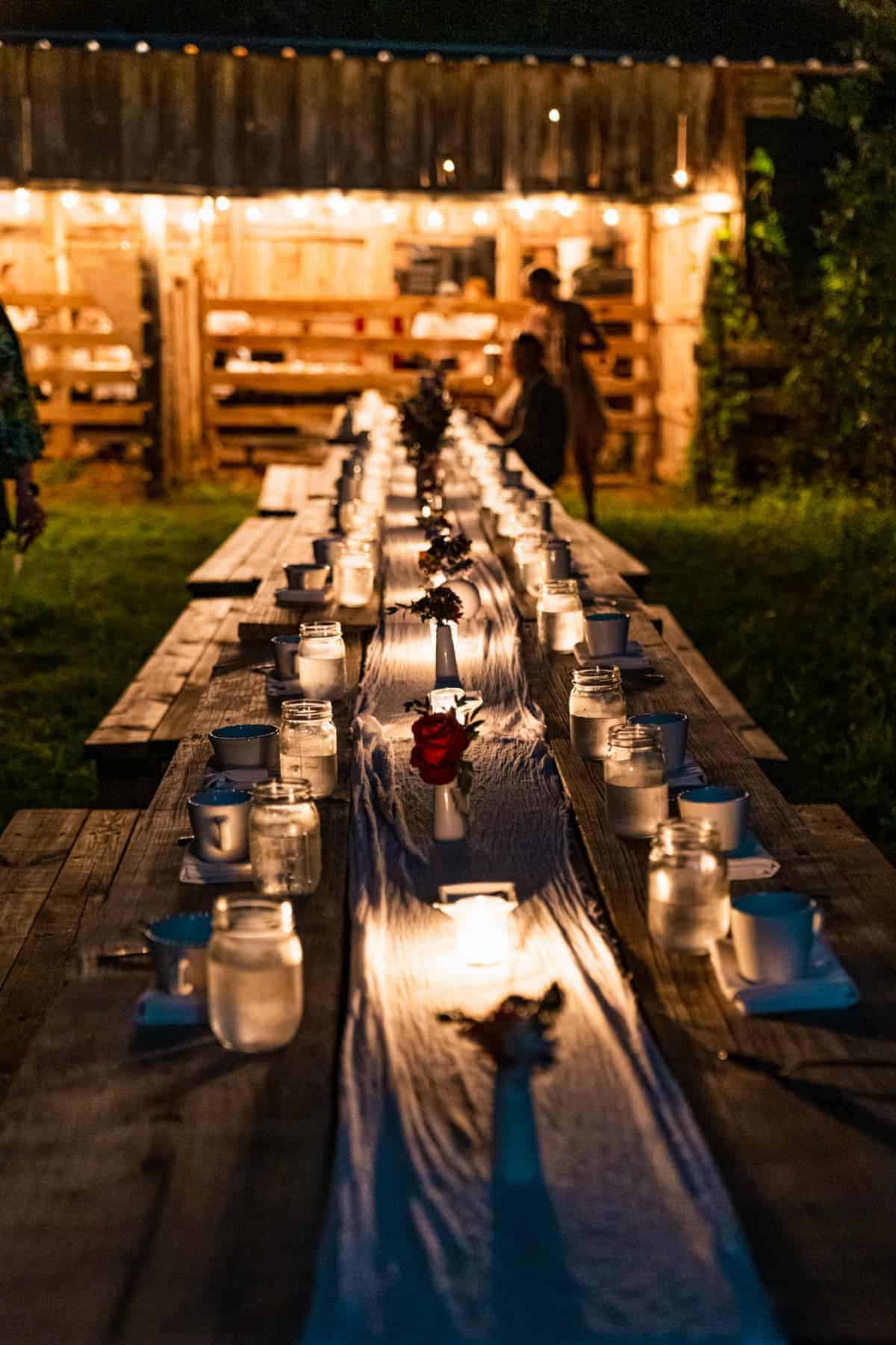 Long wooden table lit with candles and a barn in the background