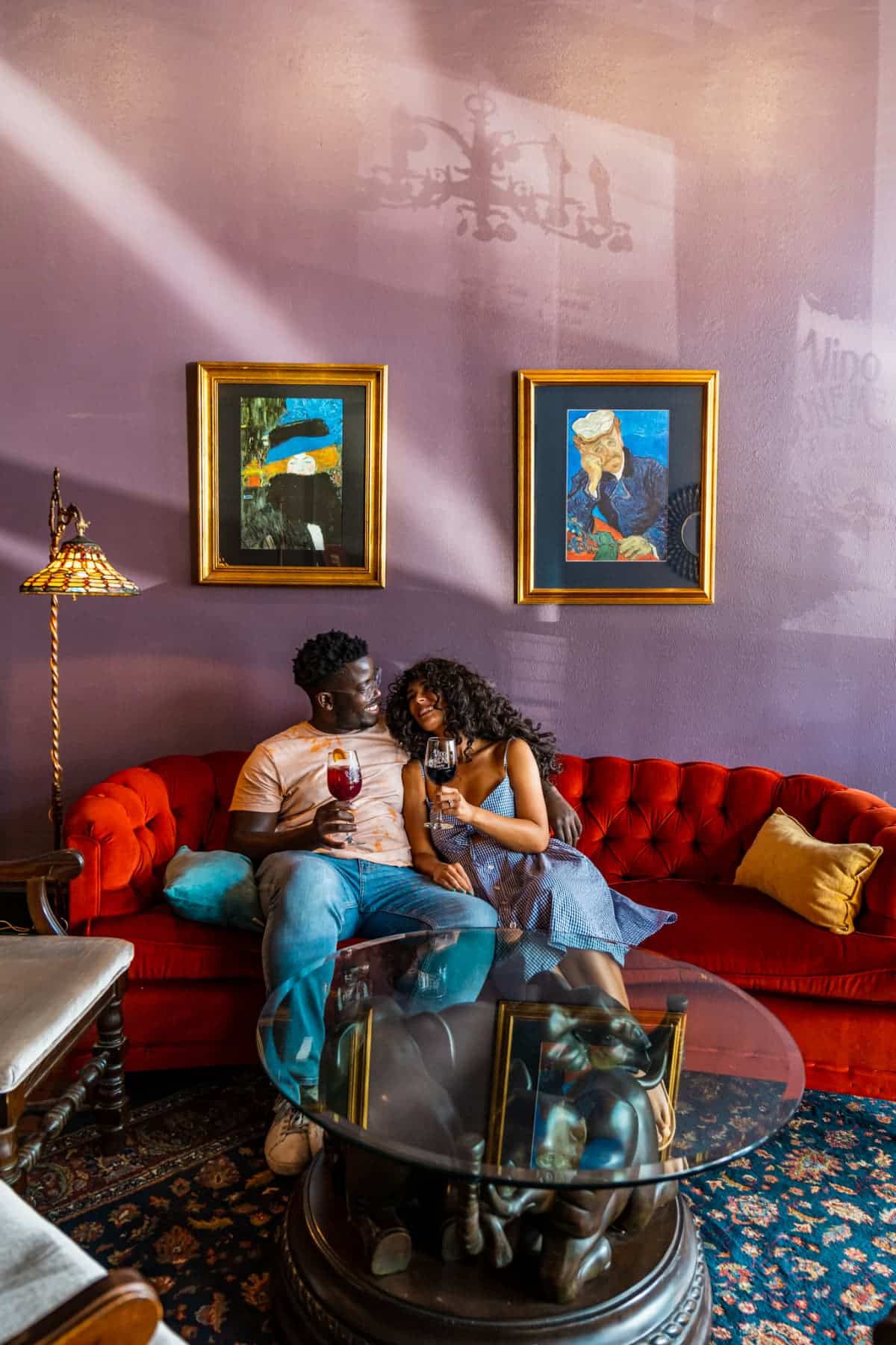 Couple holding glasses of wine on a tufted, red couch