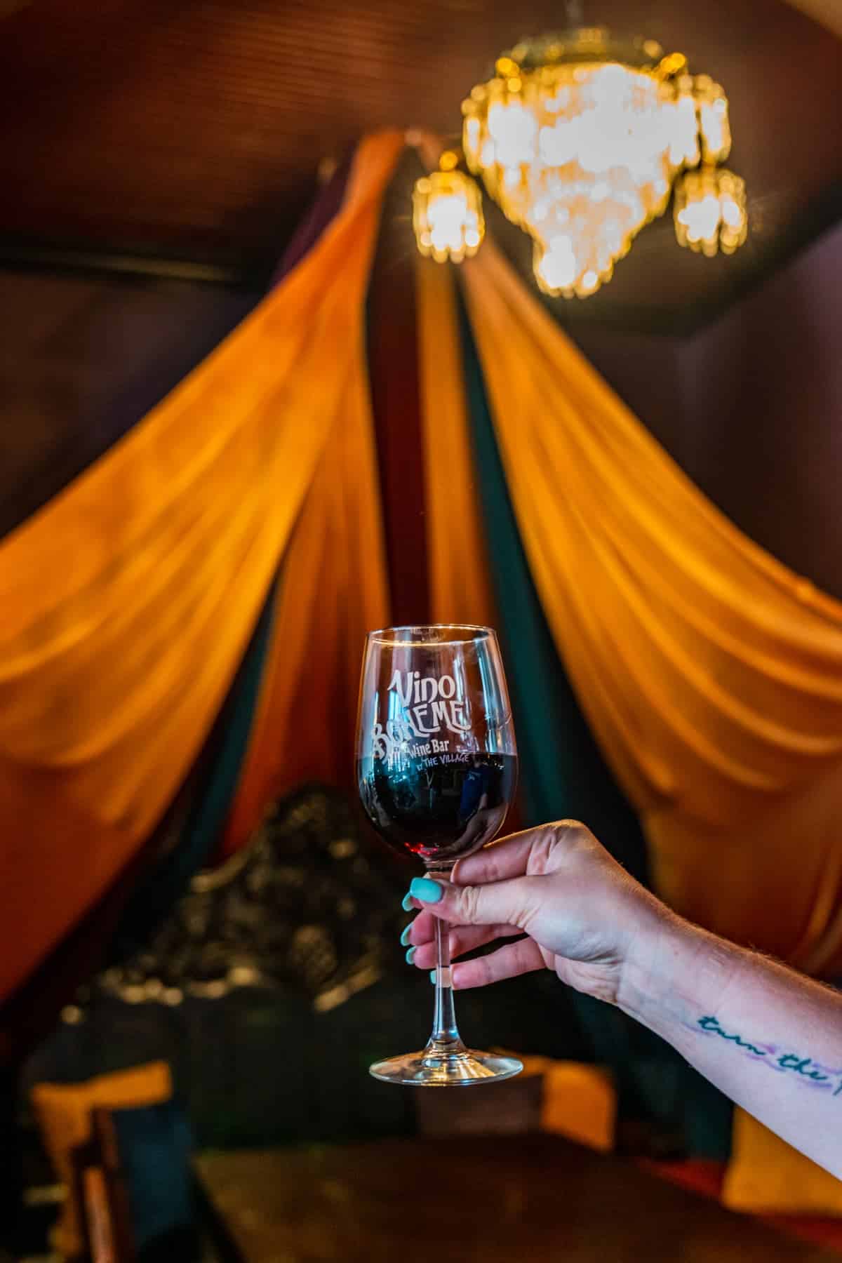 A hand holding a glass of wine in front of some yellow, red, and green curtains