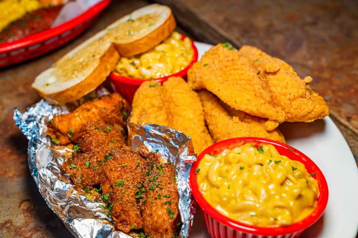 A plate of battered fish halves, wings, toast, and two small sides of mac and cheese