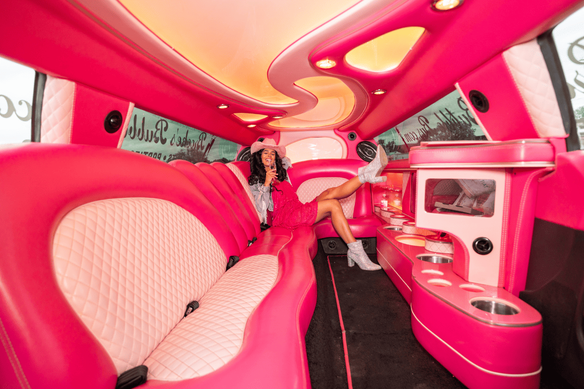 A woman sitting in the back seat of a pink limousine.