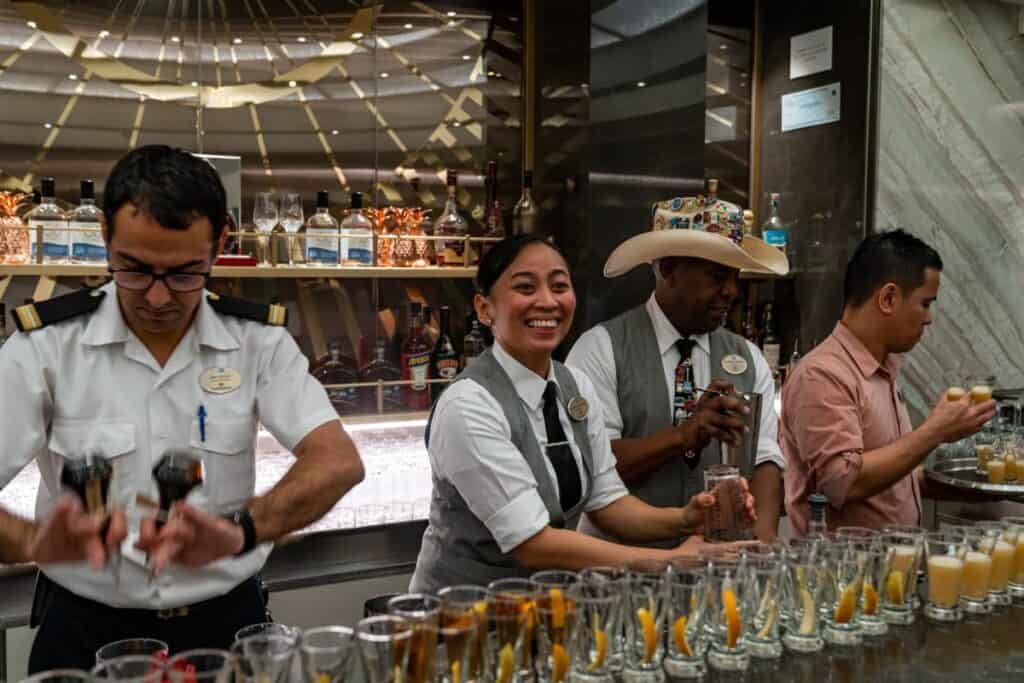 Four bartenders working with rows of cocktails in front of them