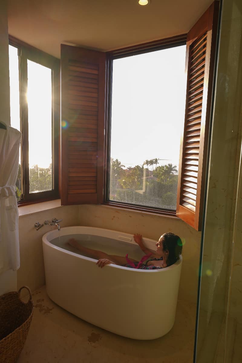 Woman in a bathtub as the sun sets with windows around her