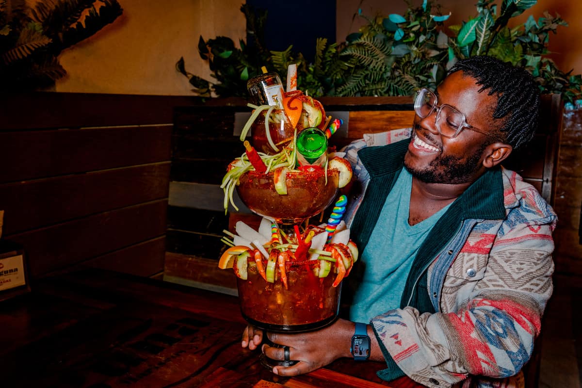 Man holding an elaborately decorated Michelada that is three glasses high