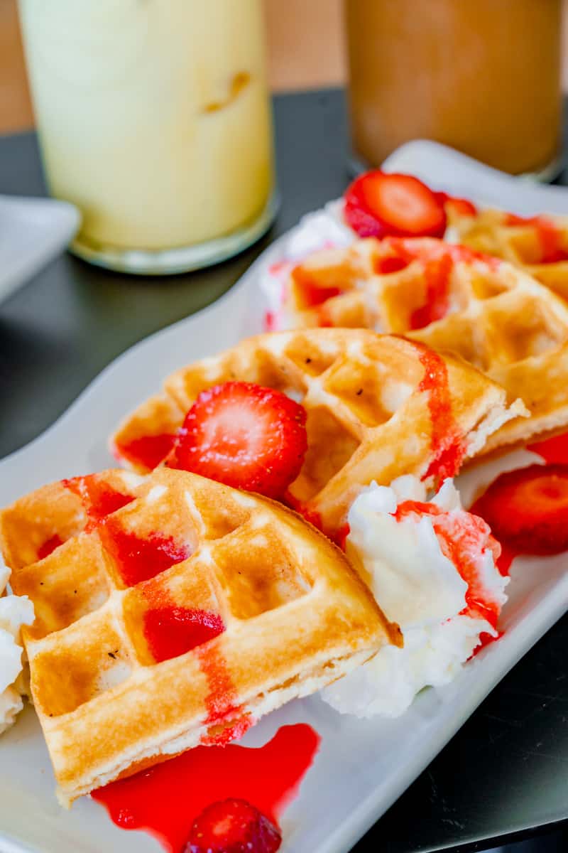 Plate of waffles with strawberry syrup, fresh strawberries, and whipped cream