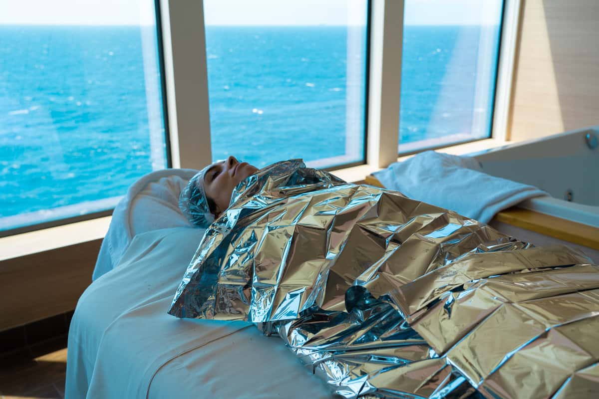 Woman laying on a massage table wrapped in foil with ocean views behind her