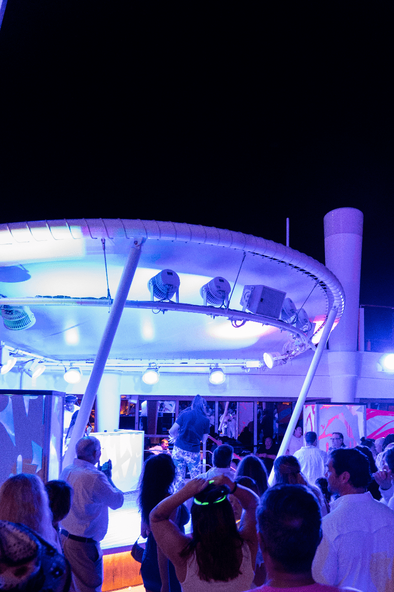 People dancing under white lights on the pool deck at a GLOW party