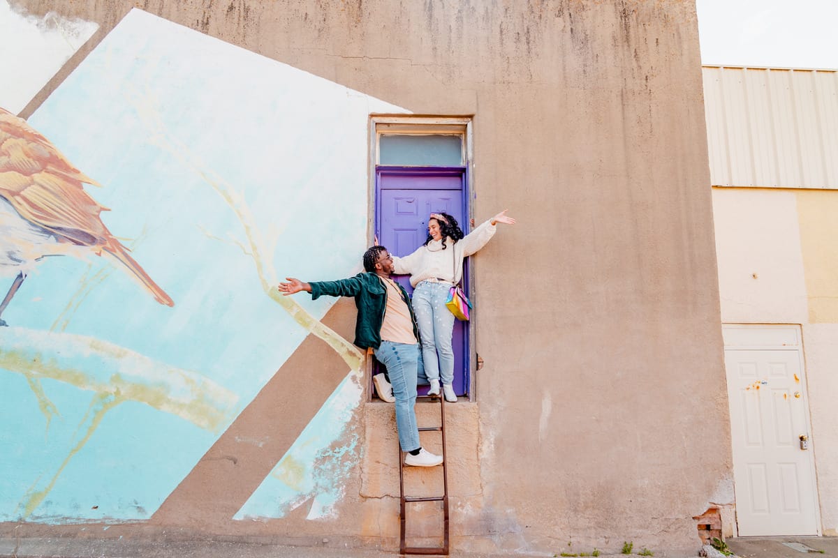 A couple posing at the top of a small ladder in front of a purple door