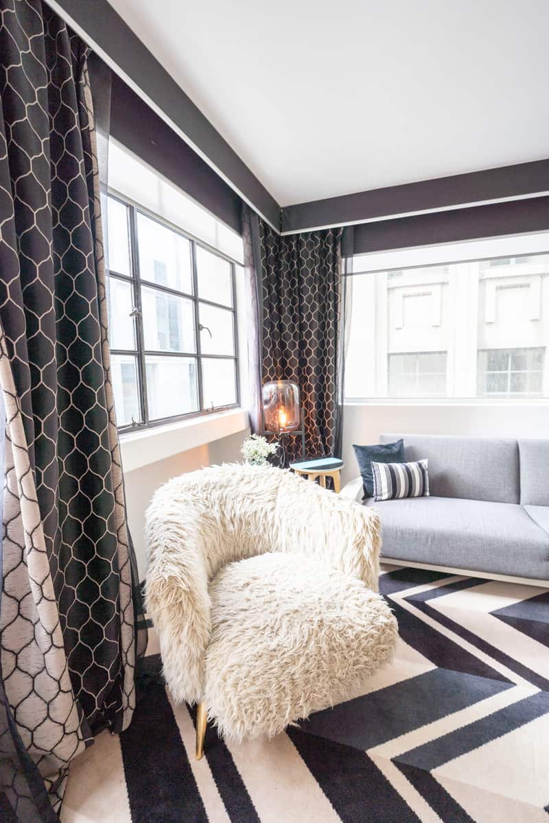 Sherpa chair, patterned curtains and gray couch inside hotel room