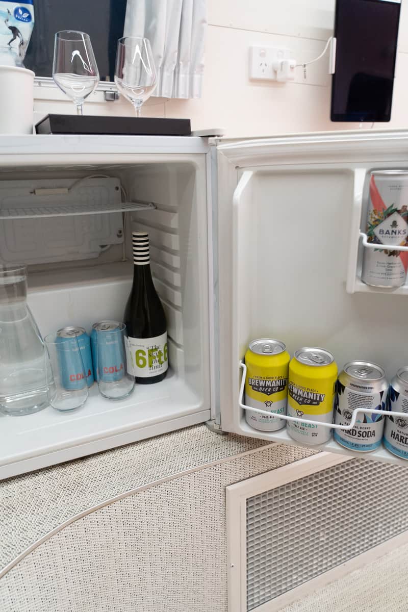A mini fridge with canned drinks and a bottle of champagne