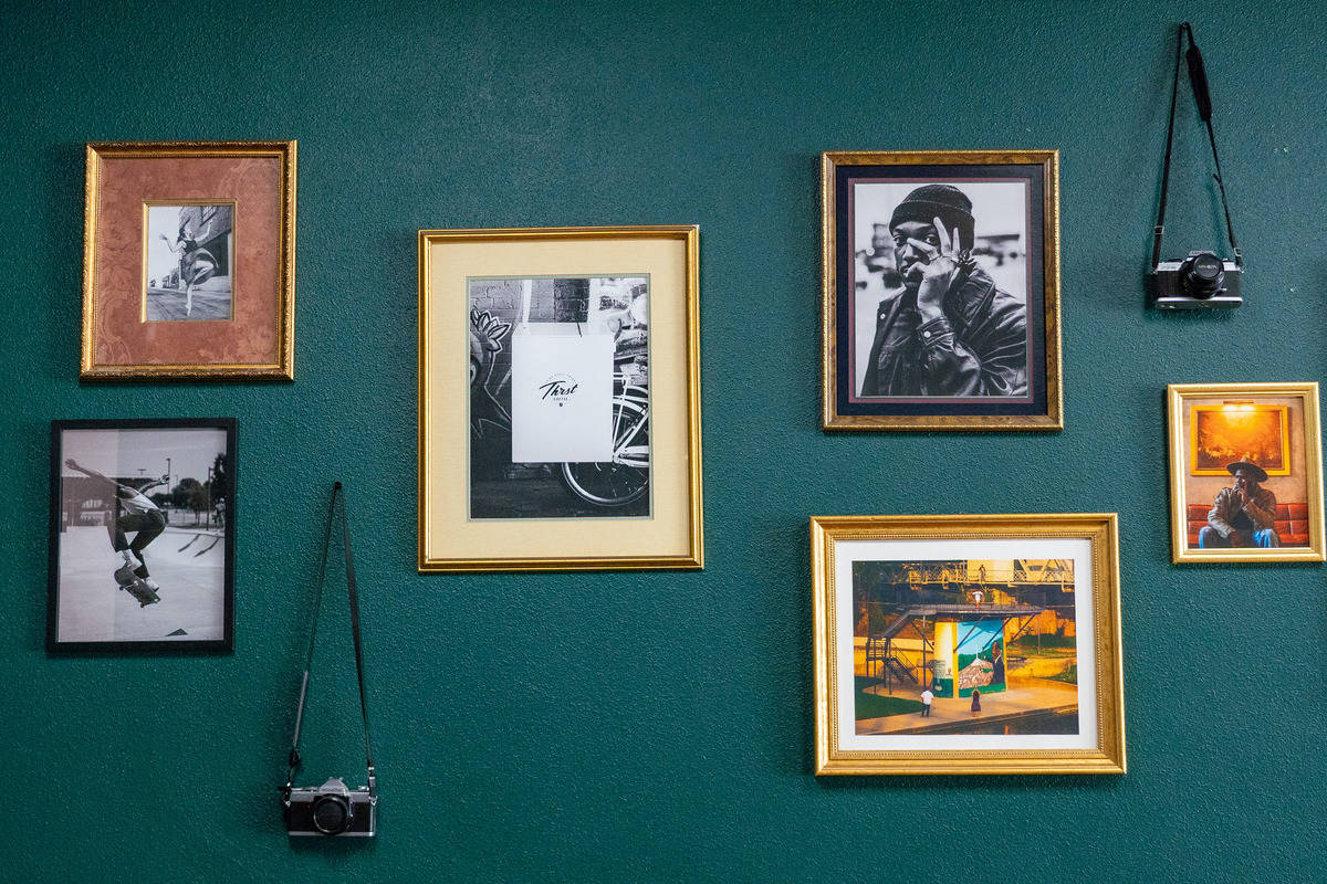 Wall with framed black-and-white & colored photographs and a camera hanging from a tack. The walls are a deep green.