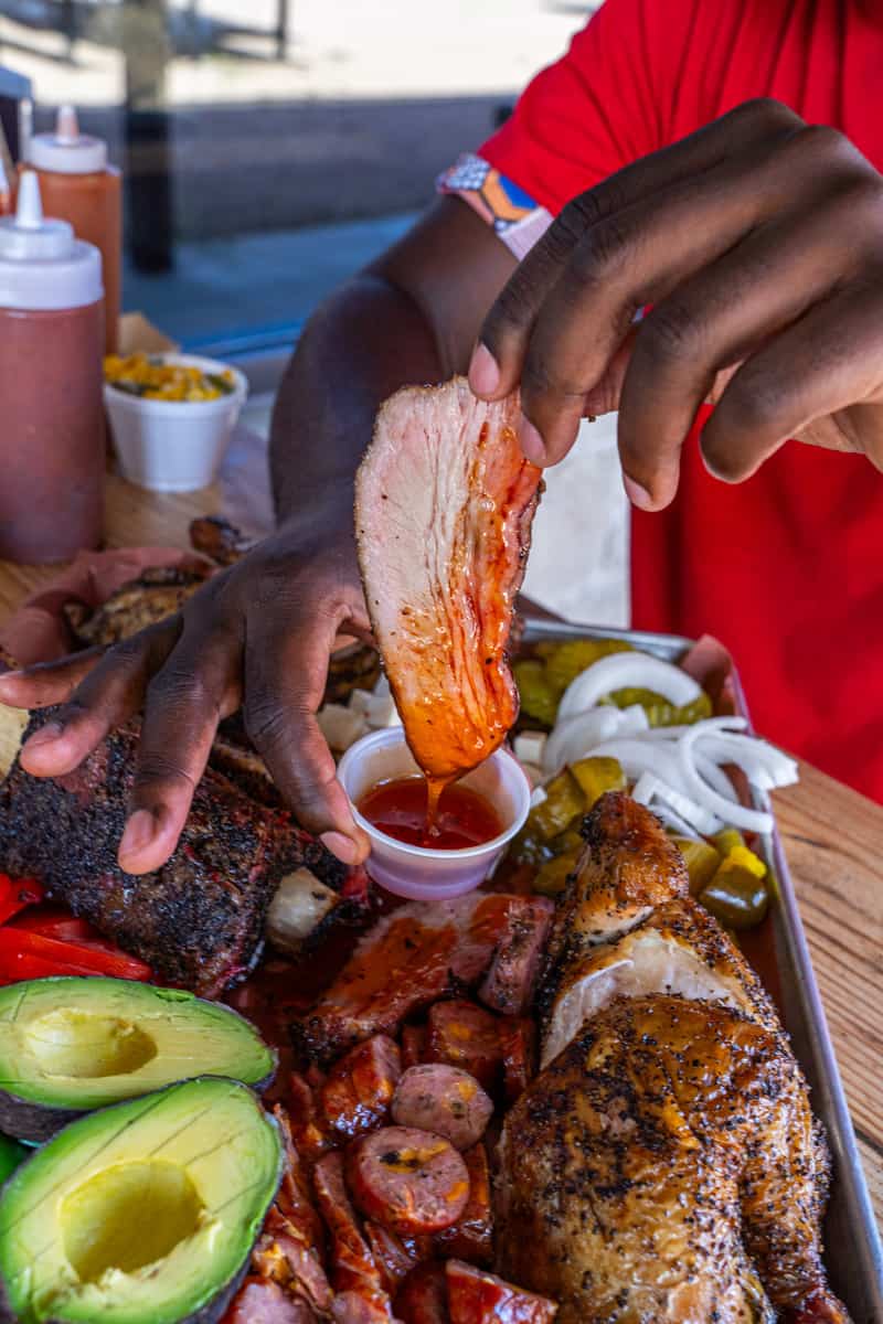 Woman dipping a piece of meat in barbecue sauce